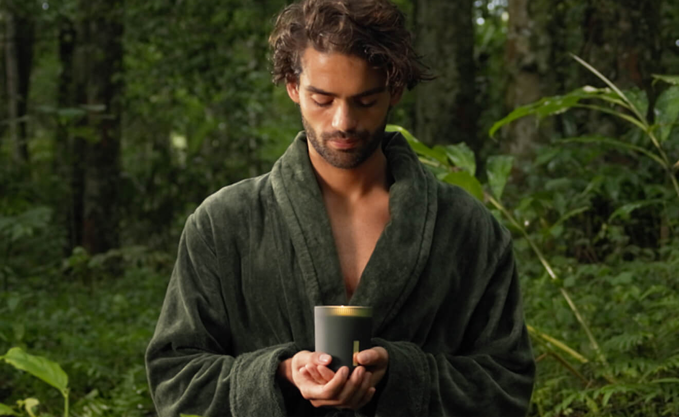 Person in green robe holding a scented candle in a lush forest setting