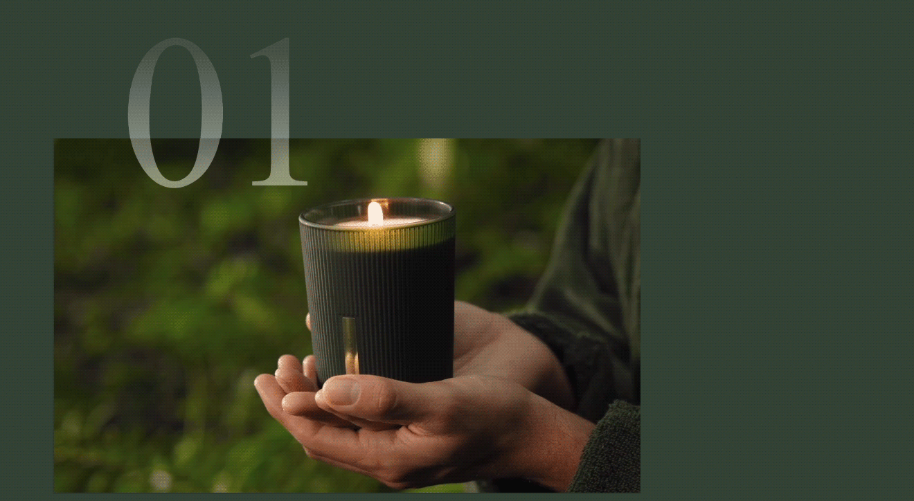 Hands cradling a lit scented candle in a dark green glass holder